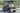 TrailMaster Taurus 50EV 4-Seat Electric Golf Cart with DOT Light Package, aluminum wheels, and off-road tires on paved road.