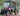 Red TrailMaster Taurus 50EV 4-Seat Electric Golf Cart with DOT lights, aluminum wheels, and off-road tires in park setting.